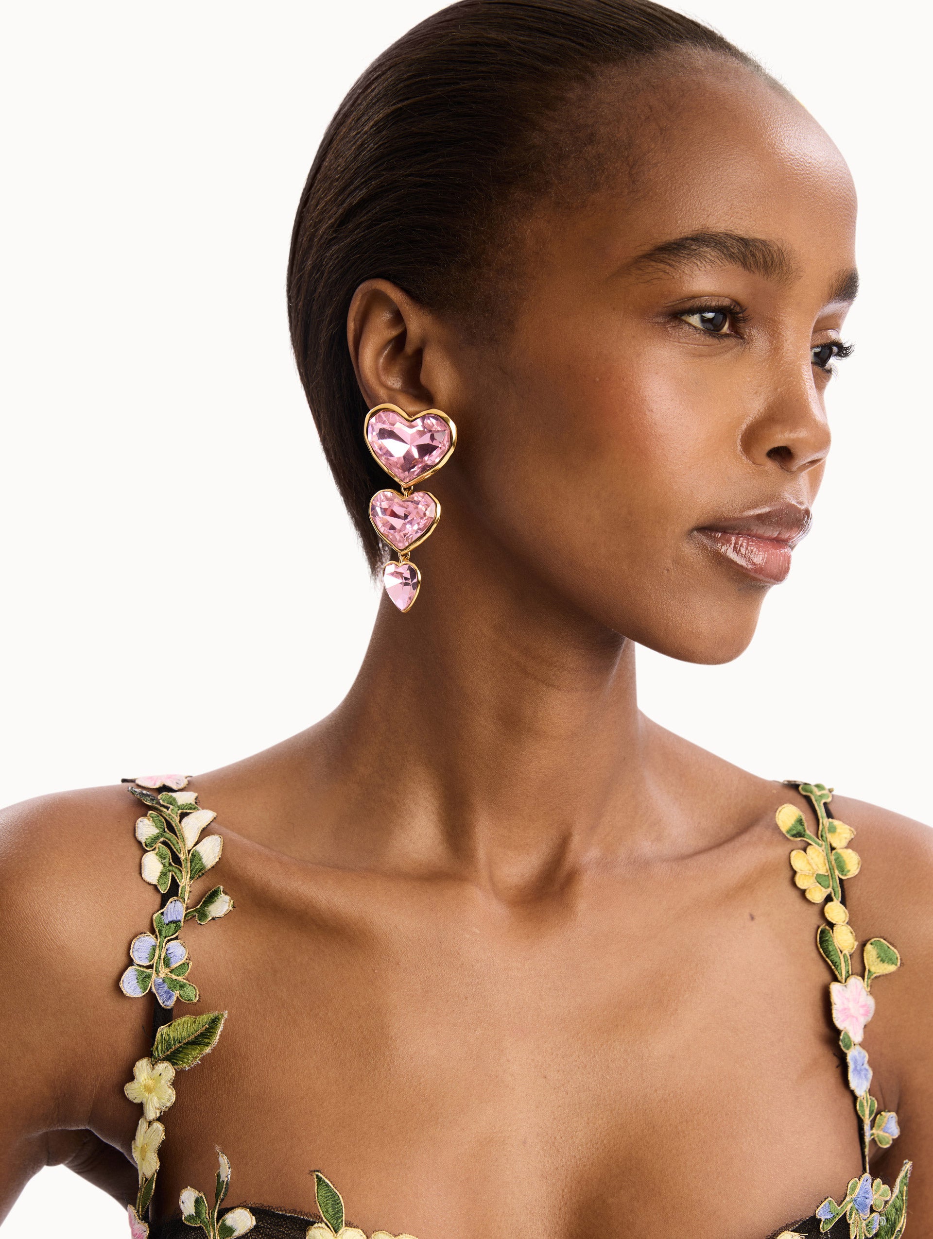 The model is wearing the Pink Crystal Heart Drop Clip-On Earrings. Three vertically connected hearts with gold rims. Detail View.