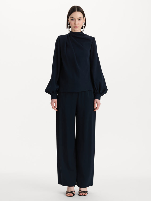 The model is wearing the Draped Georgette Blouse in the color Navy. Featuring silk georgette, a draping mock-neckline, and long, billowed sleeves. Front View.