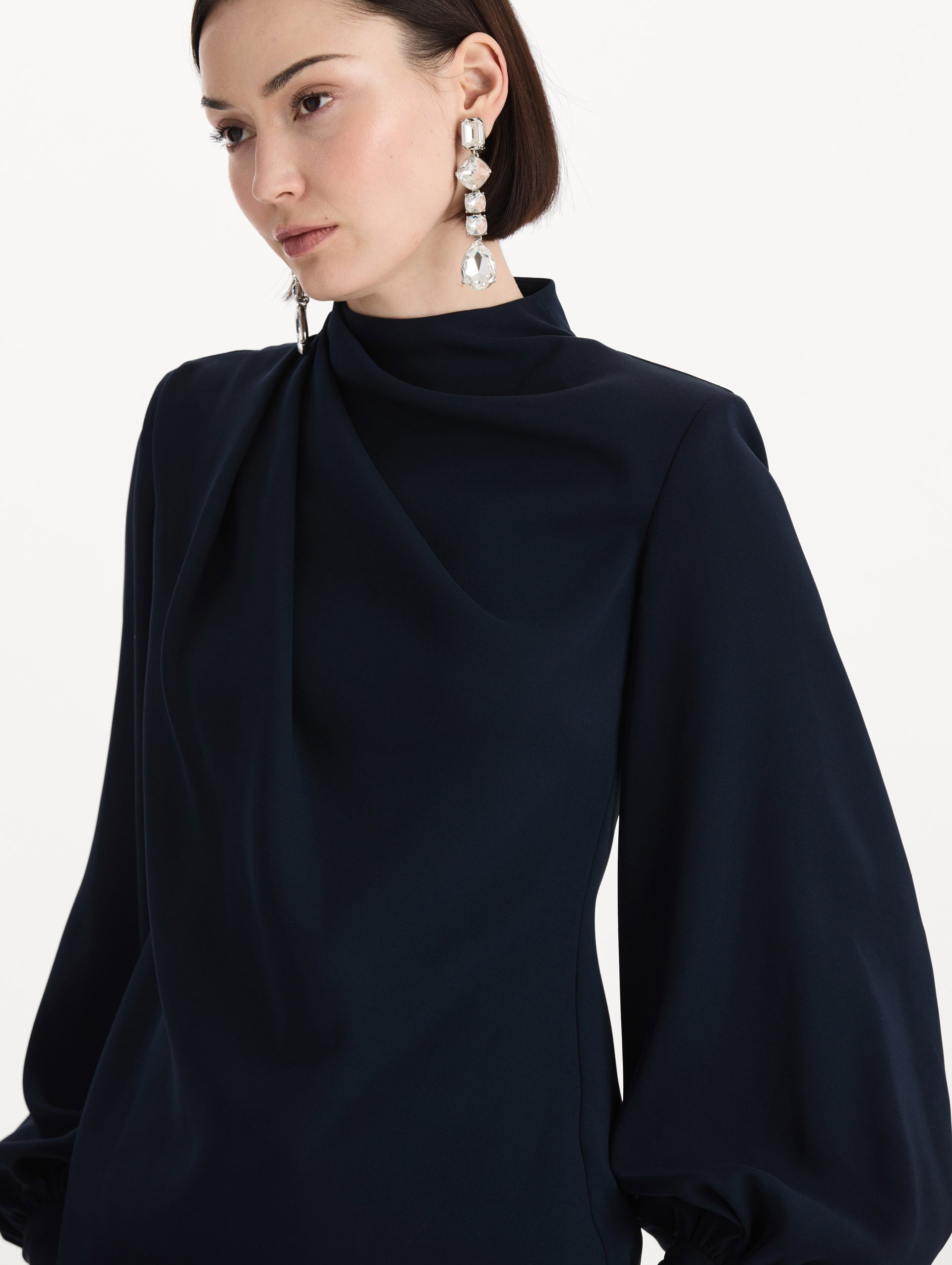 The model is wearing the Draped Georgette Blouse in the color Navy. Featuring silk georgette, a draping mock-neckline, and long, billowed sleeves. Detail Shot.