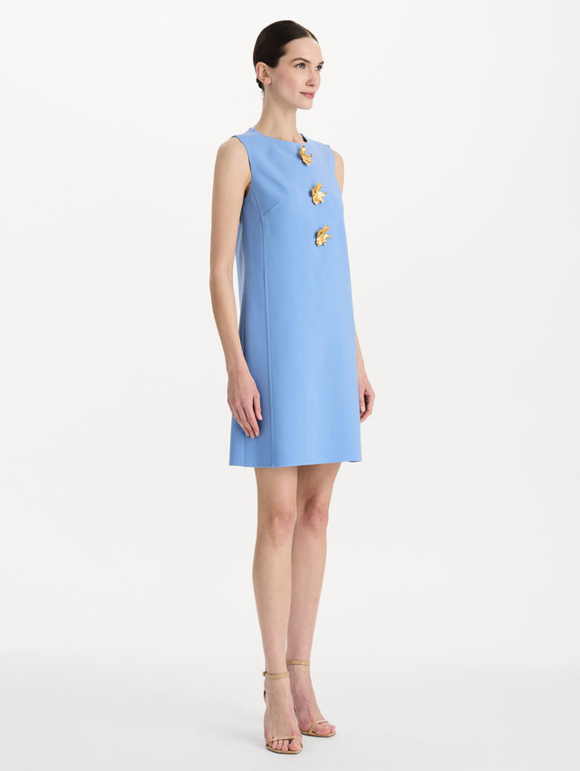 The model is wearing the Button-Detail Wool Shift Dress in the color Hydrangea blue in a mini-length, featuring bold, floral gold buttons. Side View.