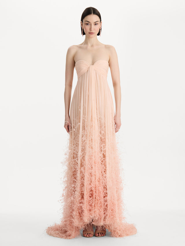 The model is wearing a strapless, sweetheart neckline gown in Blush Pink. Featuring a long flowing skirt with feather details. Front View.