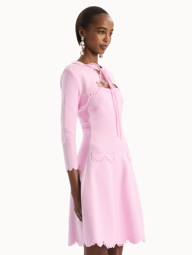 The model is wearing the Scallop Trim Knit Bolero with tie at front in the color pink. Side View.
