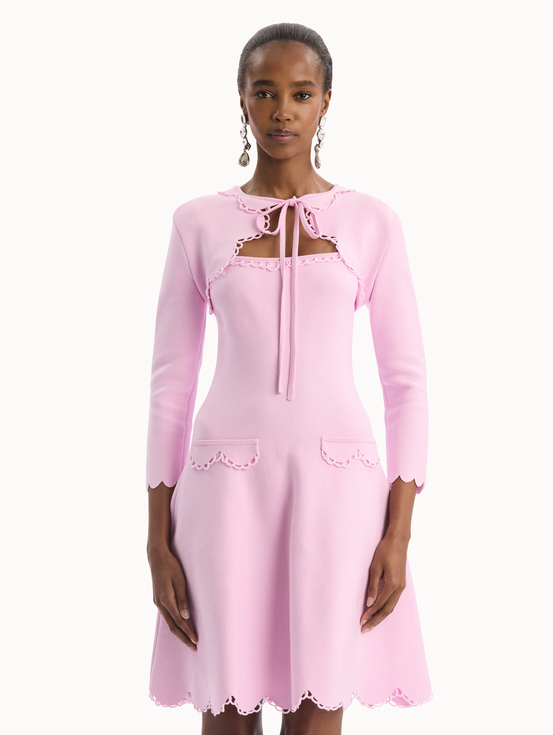 The model is wearing the Scallop Trim Knit Bolero with tie at front in the color pink. Front View.