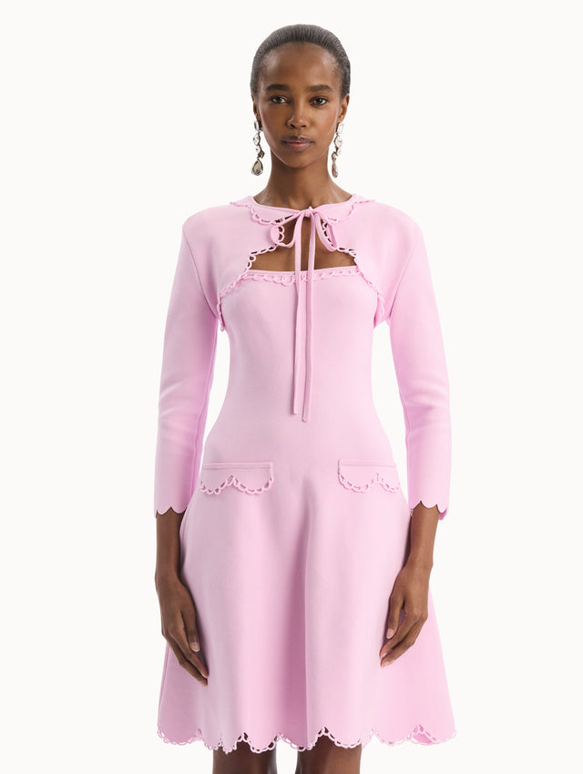 The model is wearing the Scallop Trim Knit Bolero with tie at front in the color pink. Front View.