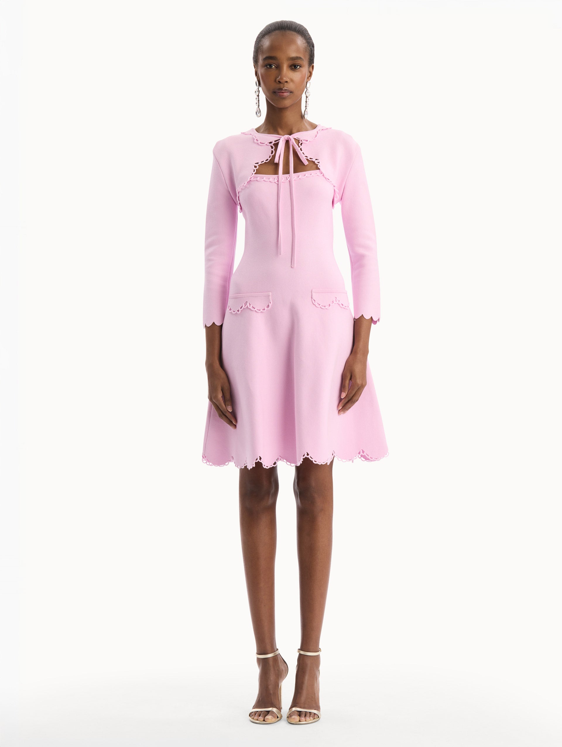 The model is wearing the Scallop Trim Knit Bolero with tie at front in the color pink. Front View.