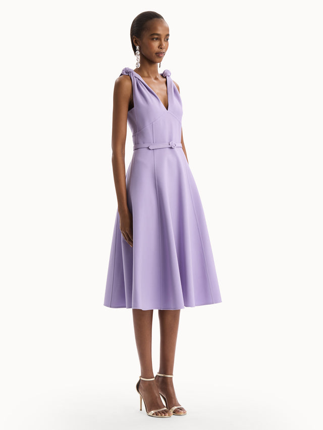 The model is wearing the Twist-Detailed Wool Dress in Purple featuring a deep V-neckline and belt at waist. Side View.
