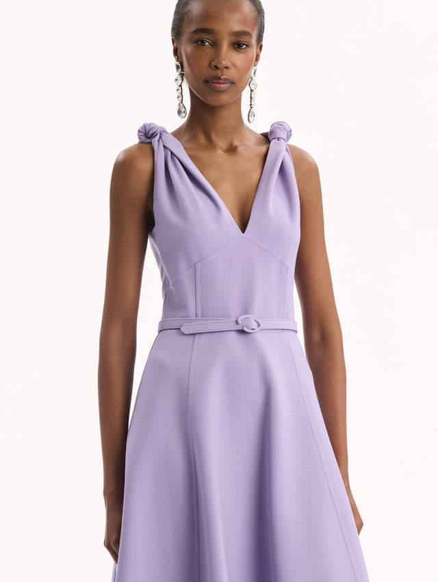 The model is wearing the Twist-Detailed Wool Dress in Purple featuring a deep V-neckline and belt at waist. Front View.