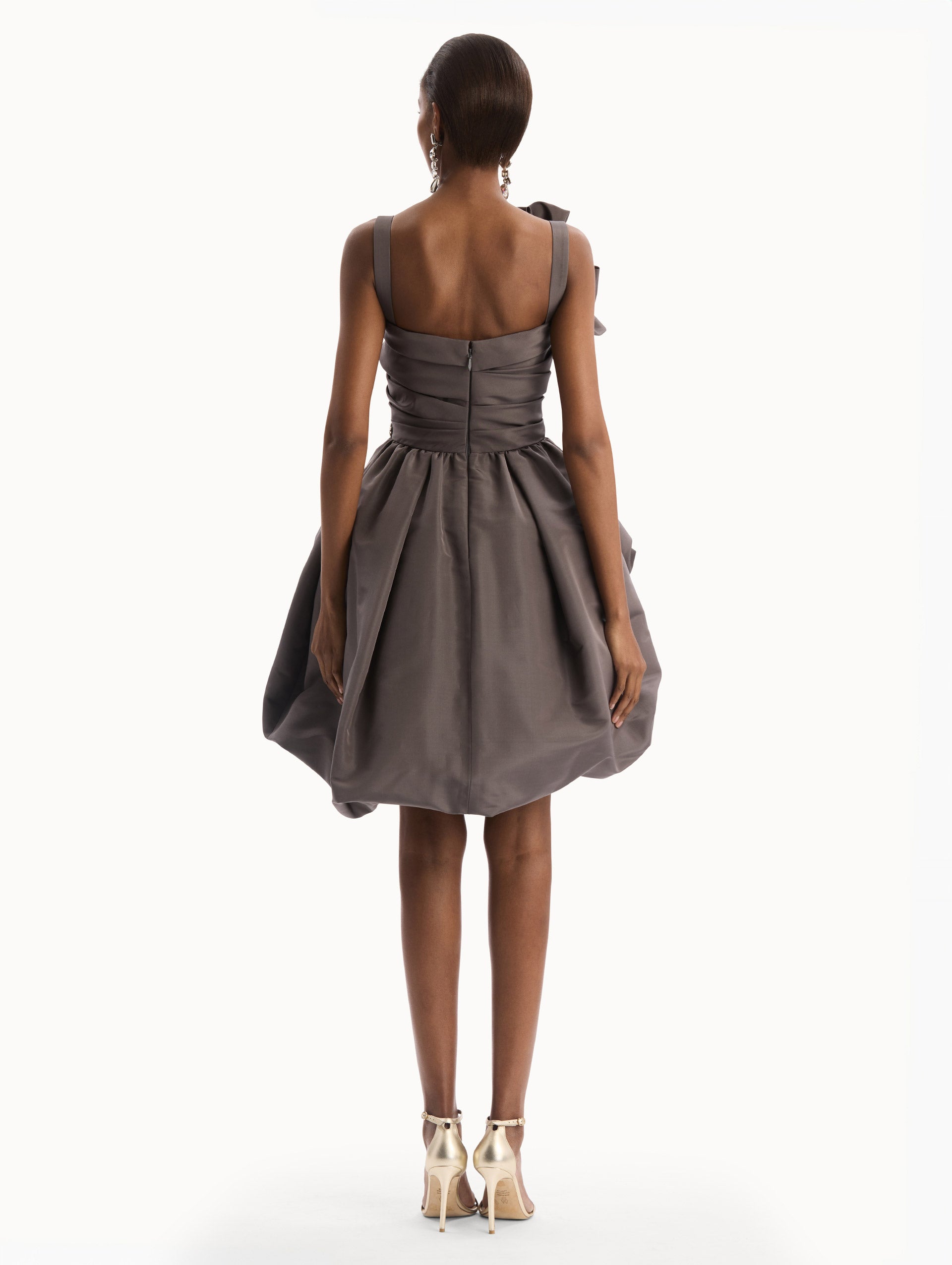 The model is wearing the Brooch Embroidered Cocktail Sleeveless Dress in a dark, grey stone color with a jeweled brooch motif, oversized shoulder bow and voluminous draped skirt. Back View.