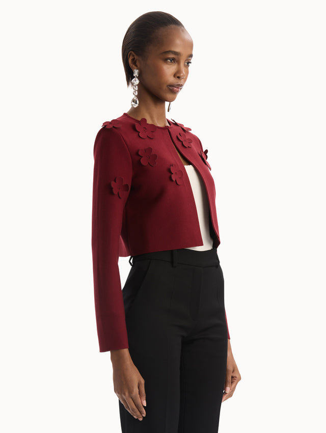The model is wearing the Laser-Cut Floral Knit Cardigan in a wine, red color with sculptural floral appliqués. Side View.