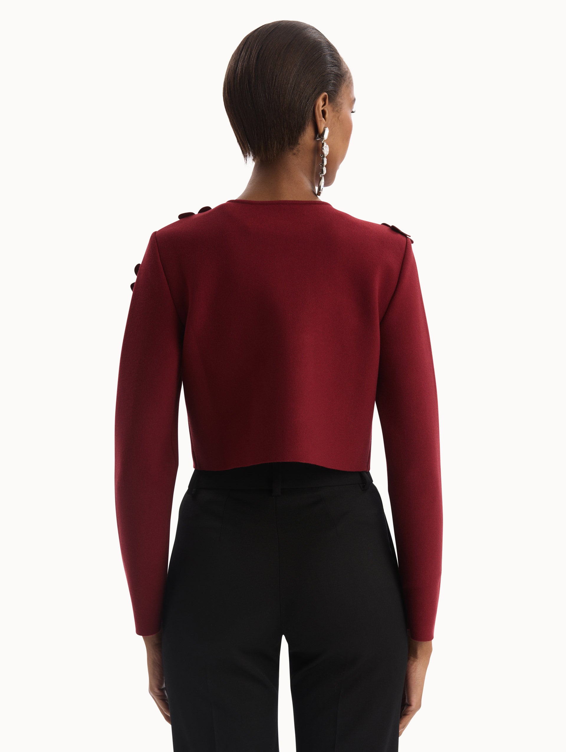 The model is wearing the Laser-Cut Floral Knit Cardigan in a wine, red color with sculptural floral appliqués. Back View.