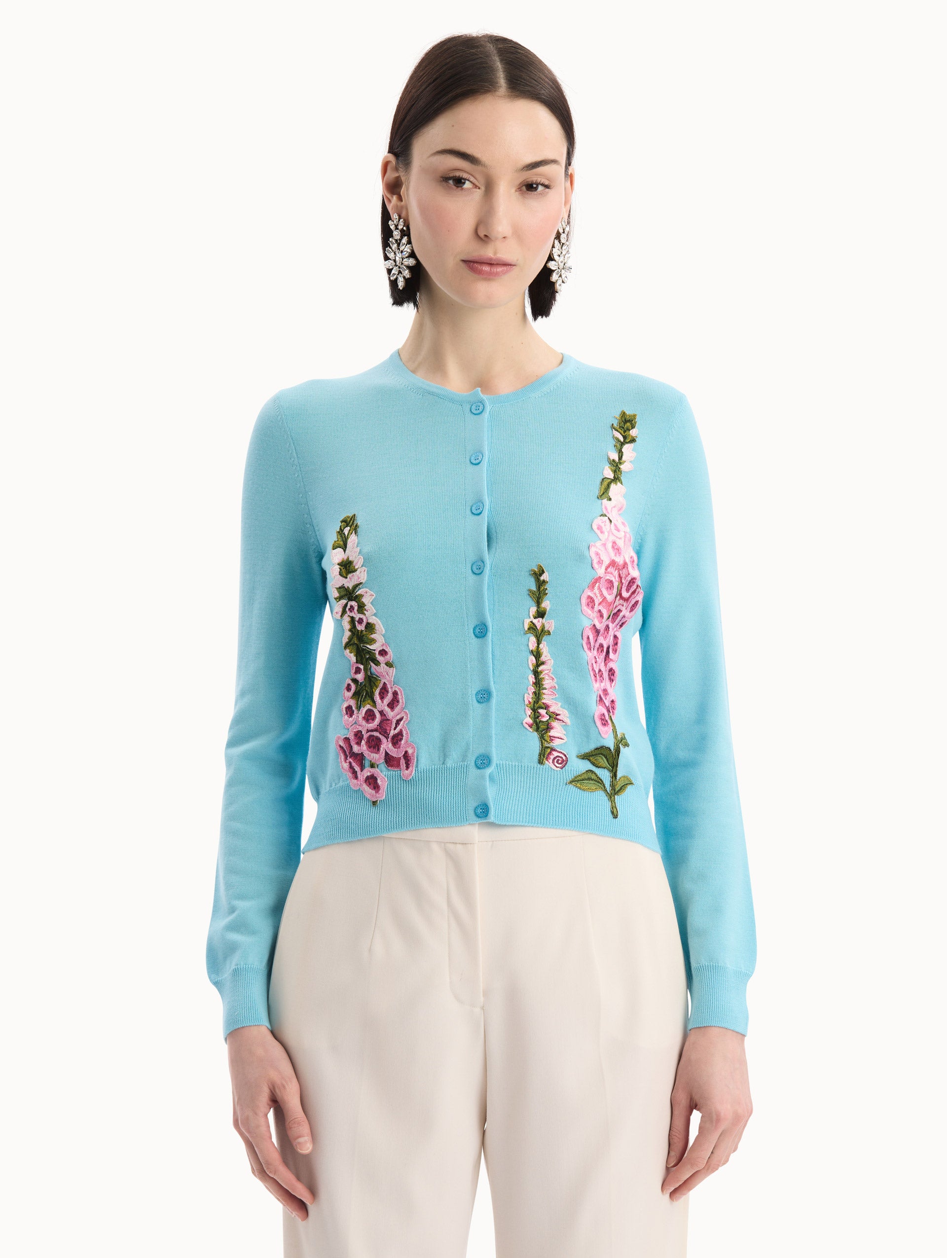 The model is wearing the Foxglove Threadwork Cardigan in vibrant light blue color with floral embroidery and buttons along the center. Front View.