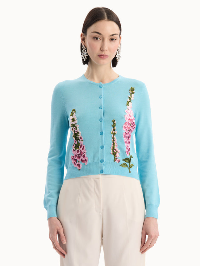 The model is wearing the Foxglove Threadwork Cardigan in vibrant light blue color with floral embroidery and buttons along the center. Front View.