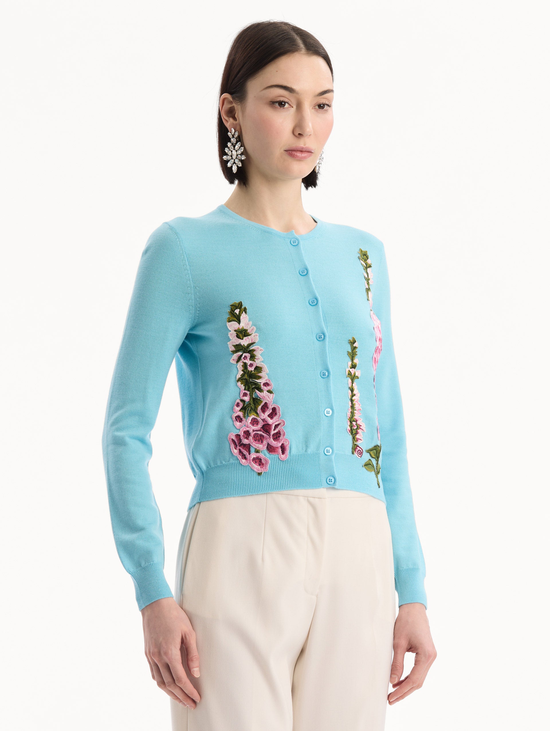 The model is wearing the Foxglove Threadwork Cardigan in vibrant light blue color with floral embroidery and buttons along the center. Side View.
