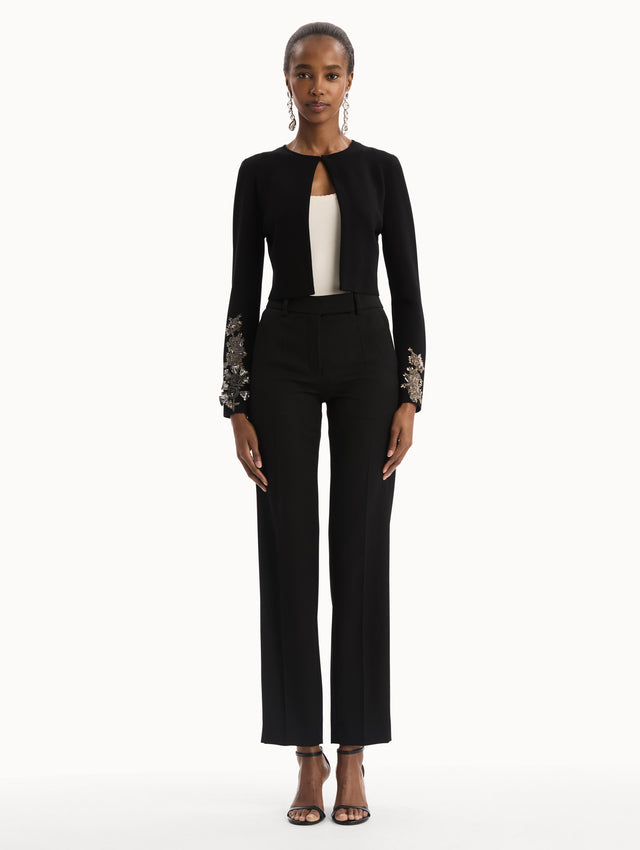 The model is wearing the Black Feather Sequin Embroidered Knit Cardigan featuring an open front, textured inset panel, and silver floral embroidery along the sleeves. Front View.