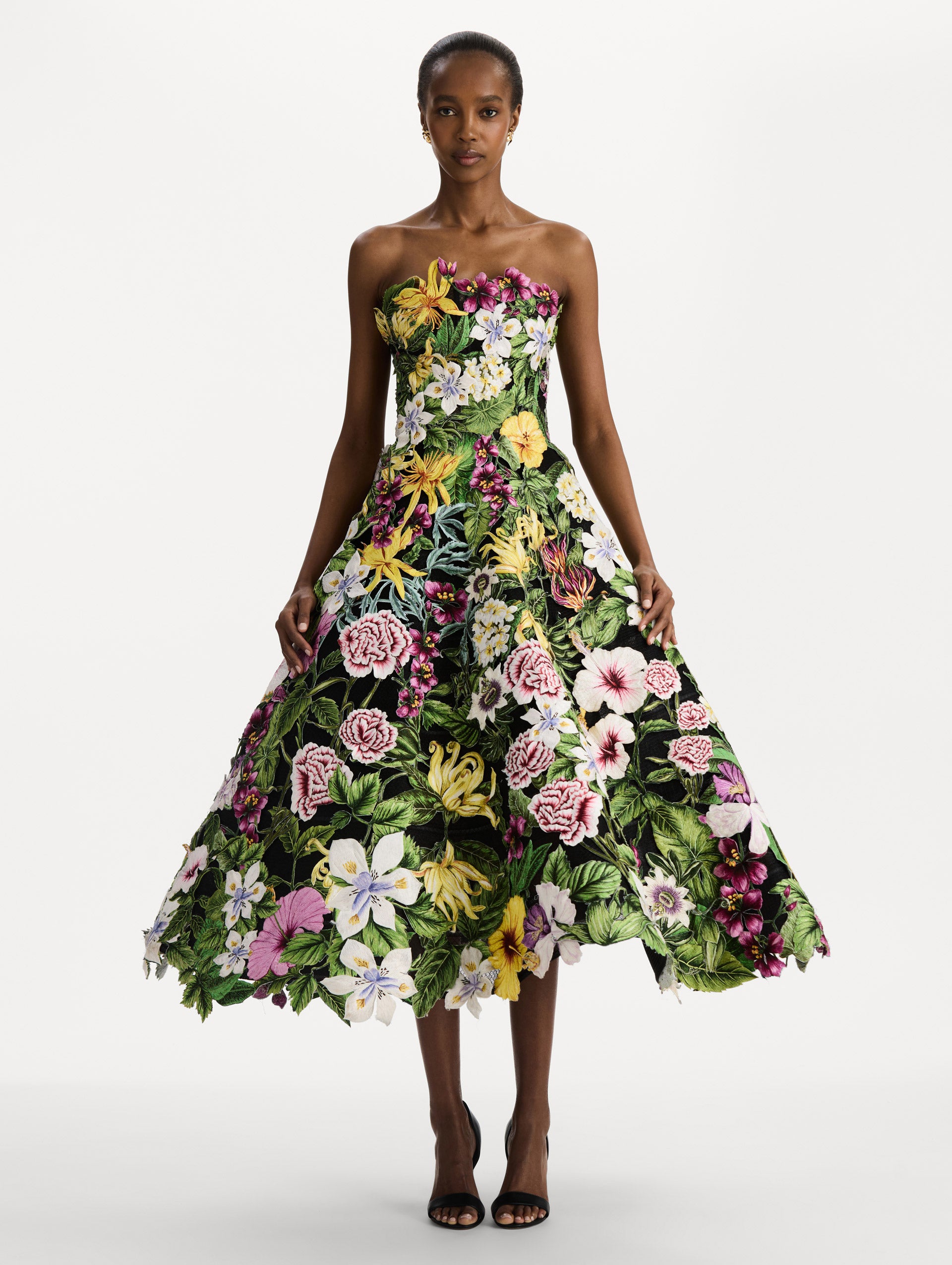 The model is wearing the Dominican Mixed-Floral Guipure Gown. Featuring a strapless neckline, fitted bodice, and full skirt. Front View.