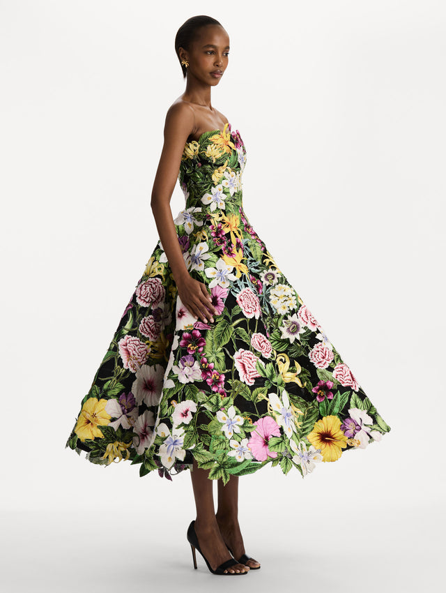 The model is wearing the Dominican Mixed-Floral Guipure Gown. Featuring a strapless neckline, fitted bodice, and full skirt. Side View.