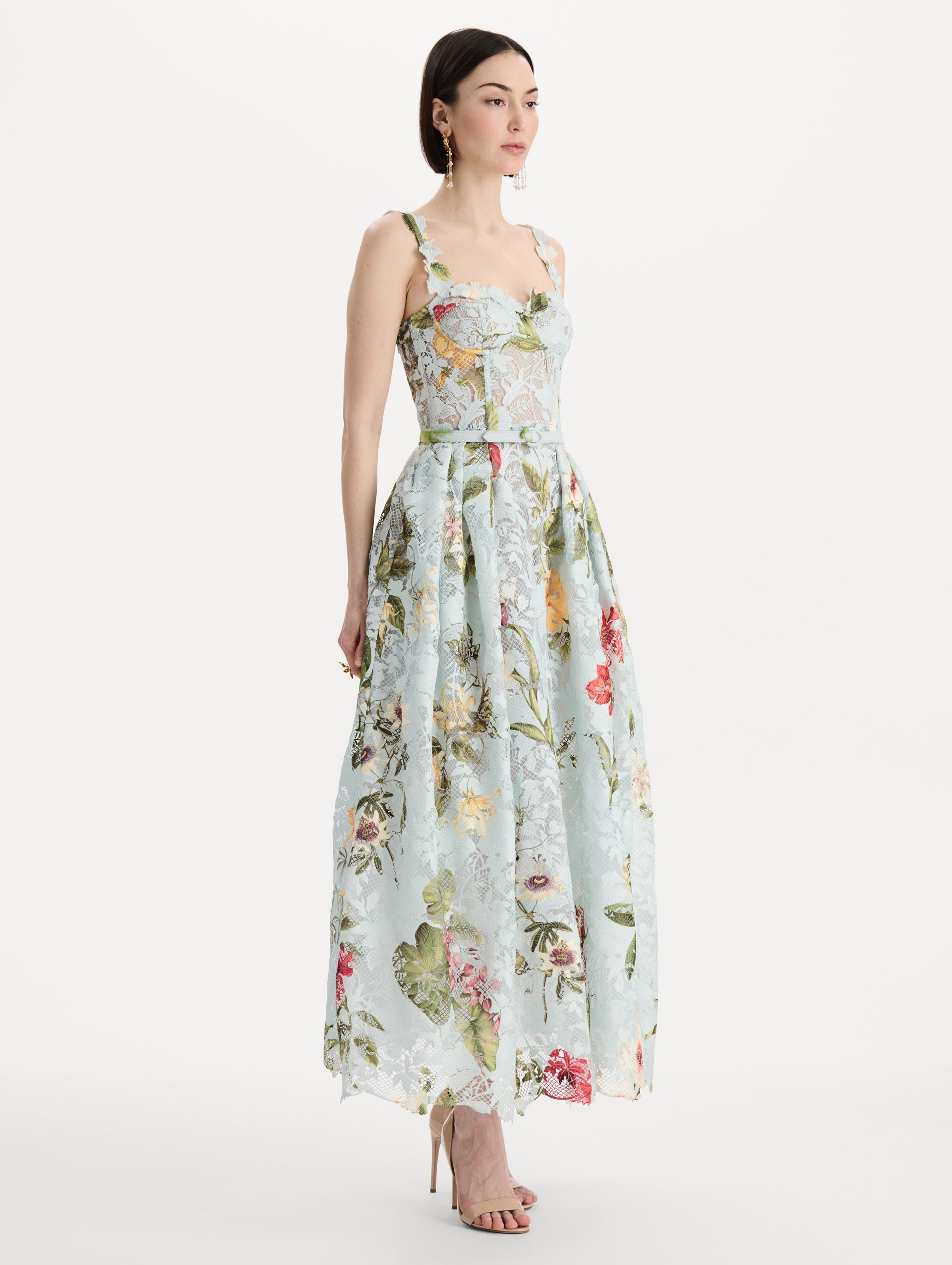 The model is wearing the Dominican Mixed-Floral Guipure Cocktail Dress in Saltwater Blue. Featuring floral detailing on straps, sweetheart neckline, structured bodice, and full skirt. Side View.