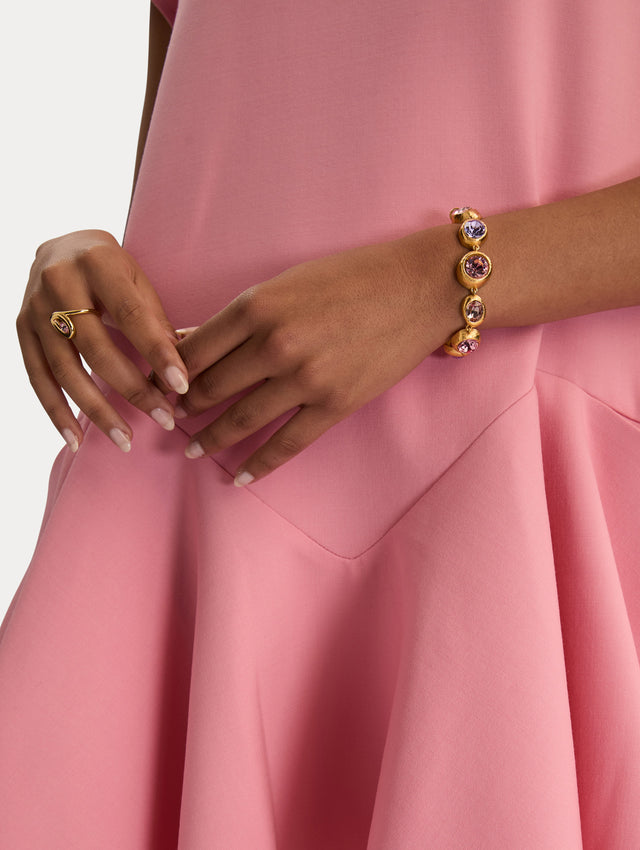 Gold Looped Oval Ring with a sculptural wave design, set with a round pink crystal at the center. Side View.