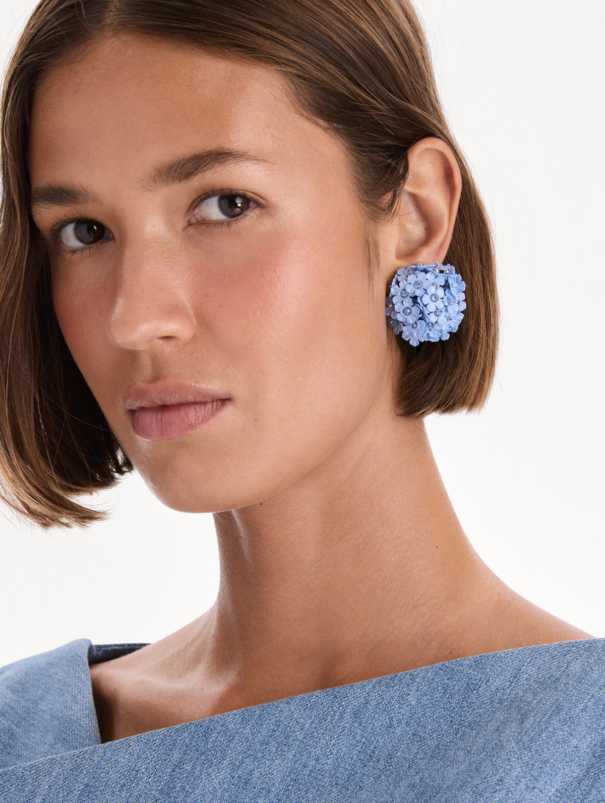 The model is wearing flower pompom small earrings. Front view.