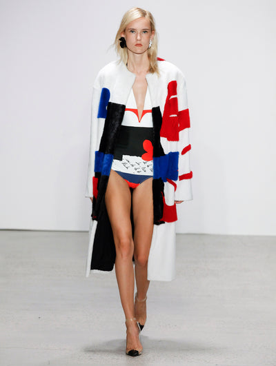 The model walks the runway in a color-blocked fur jacket of white, red, blue and black with a coordinating bodysuit of the same color and pattern.