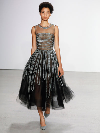 The model walks the runway in a semi-sheer black tulle illusion-neck cocktail dress, adorned with sinuous silver sequin embroidery.
