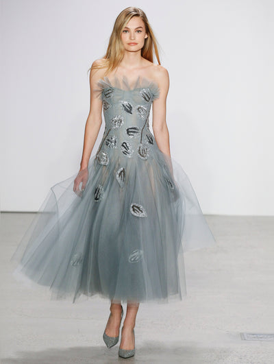 The model walks the runway in a soft blue tulle strapless cocktail dress adorned organic forms made of silver and black shimmering embroidery.