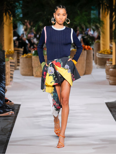 A model wears a navy sweater and multicolor floral printed black shorts