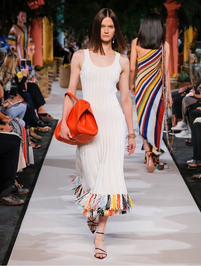A model wears a white dress with rainbow fringe at the hem
