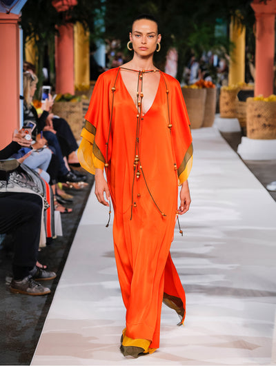 A model wears an orange caftan with yellow and brown stripes at the bottom and sleeves