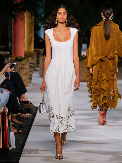 A model wears a white dress with floral cut outs at the bottom