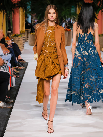 A model wears a bronze dress with lace and bow with a brown blazer