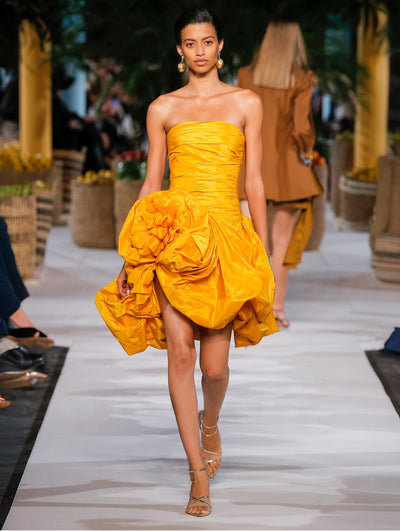A model wears a yellow dress with a big flower embroidered on the skirt