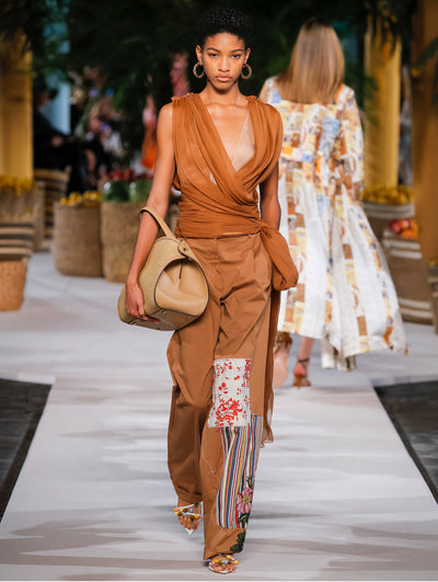 A model wears brown pants with colorful embroidery and brown tulle top