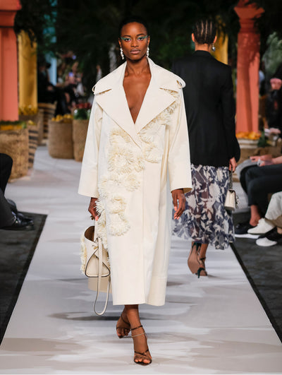 A model wears a white coat with raffia embroidery