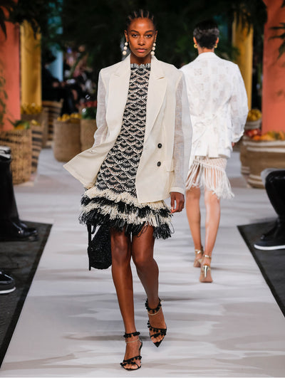 A model wears a black and nude raffia dress with white blazer