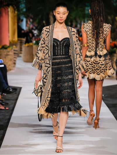 A model wears a black raffia dress and black and nude raffia coat